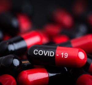 Black and red capsules in a pile with top one labelled 'COVID-19' in white writing - idea of a tablet/pill COVVID-19 vaccine