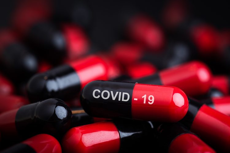 Black and red capsules in a pile with top one labelled 'COVID-19' in white writing - idea of a tablet/pill COVVID-19 vaccine