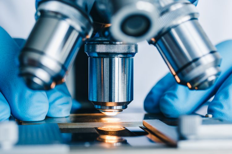 Close up of a light microscopy being used by a researcher - image shows just the metal lens and table with slide on