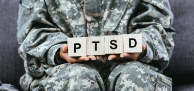 cropped shot of female soldier in military uniform sitting on sofa and holding wooden cubes with PTSD sign