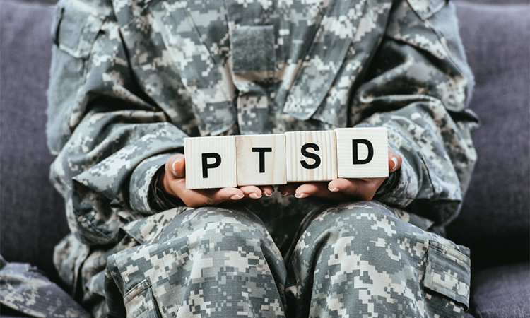 cropped shot of female soldier in military uniform sitting on sofa and holding wooden cubes with PTSD sign