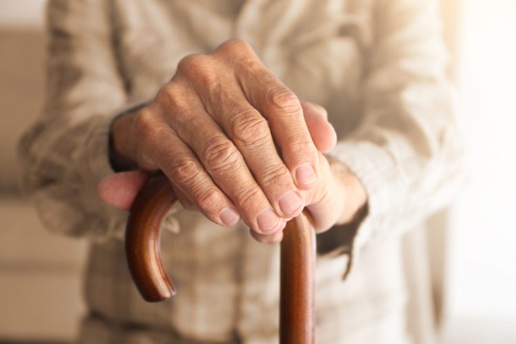close up of an old person's hands holding a walking stick - idea of age-related diseases/disorders