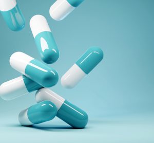 A group of white and blue antibiotic pill capsules falling on a blue background.