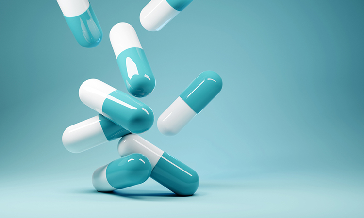 A group of white and blue antibiotic pill capsules falling on a blue background.