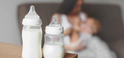 Bottles with breast milk on the background of mother holding in her hands and breastfeeding baby. Maternity and baby care.