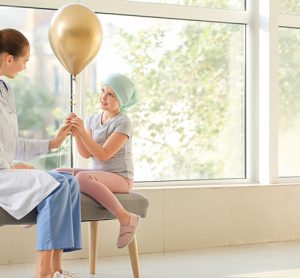 Doctor and little girl with golden balloon in clinic. Childhood cancer awareness concept
