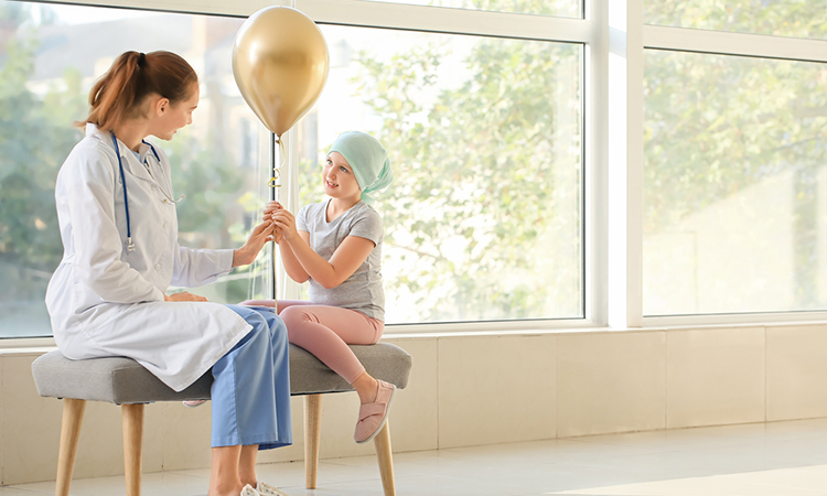 Doctor and little girl with golden balloon in clinic. Childhood cancer awareness concept