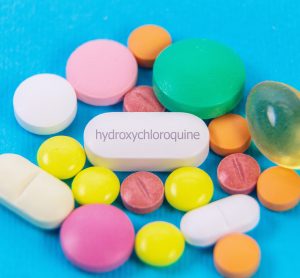 pile of colourful medication tablets with a central white tablet labelled 'hydroxychloroquine'