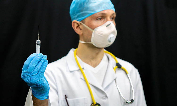 A doctor in a white coat and a coronavirus vaccine in his hand.