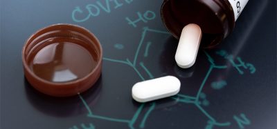 COVID-19, Corona virus flu dose of medicine or treatment drug concept, white pill tablet from medicine bottle on chemical compound on blackboard with the headline COVID-19.