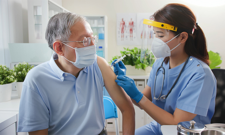 nurse wearing gloves and isolation mask is preparing a coronavirus vaccination in the shoulder of senior patient at hospital