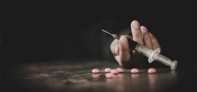 A drug addict reaches for another dose of the heroin in the syringe. Hand surrounded by pink pills.