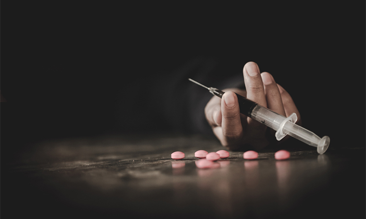 A drug addict reaches for another dose of the heroin in the syringe. Hand surrounded by pink pills.