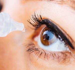 close up of woman administering eye drops to her left eye