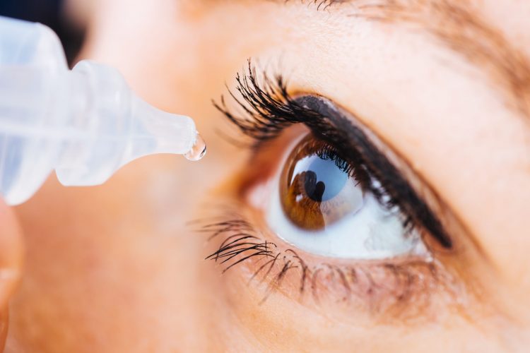 close up of woman administering eye drops to her left eye