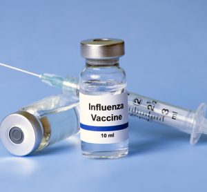 Flu vaccine, syringe, and vials on light blue background