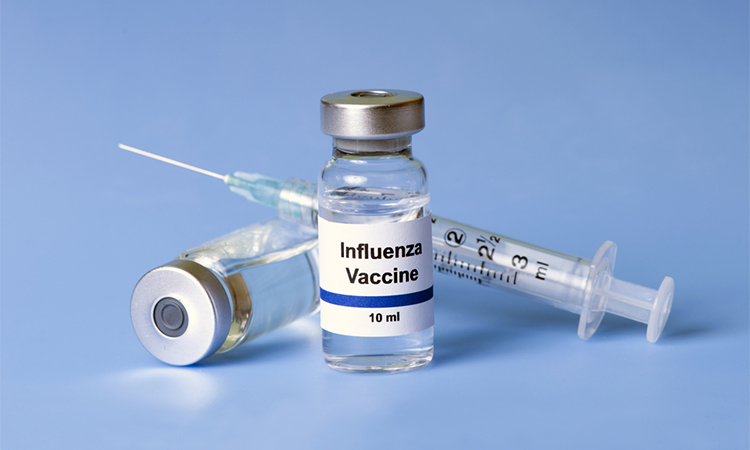 Flu vaccine, syringe, and vials on light blue background