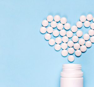 Medicine pills in shape of heart on blue background with copy space. Concept of treatment of heart disease, health care.