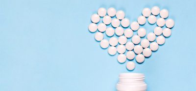 Medicine pills in shape of heart on blue background with copy space. Concept of treatment of heart disease, health care.
