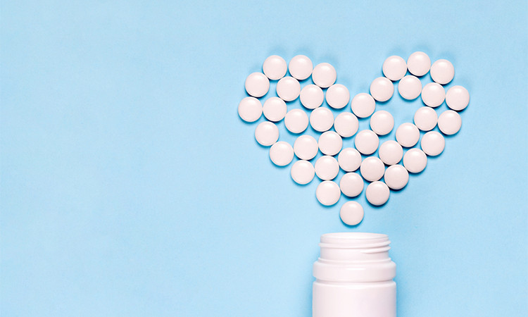Medicine pills in shape of heart on blue background with copy space. Concept of treatment of heart disease, health care.