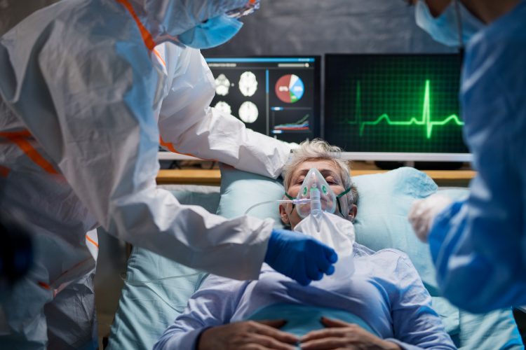 patient on a ventilator surrounded by monitors and doctors wearing personal protective equipment