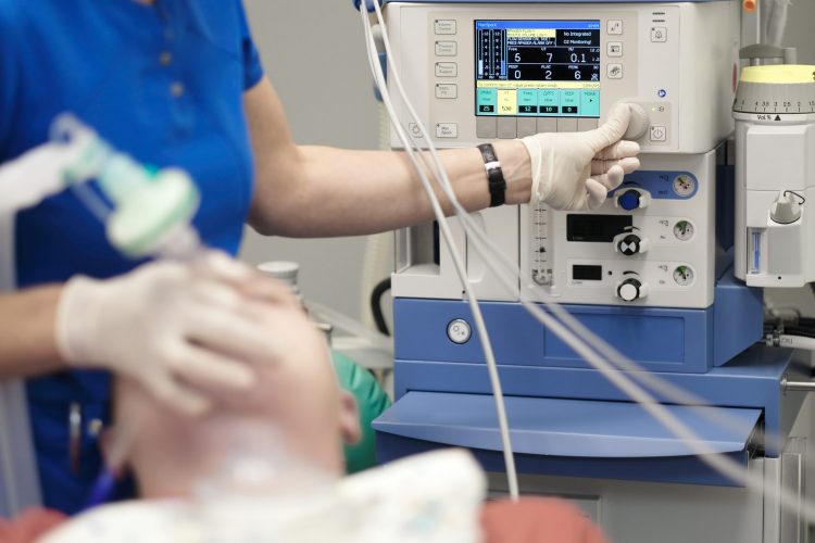 anaesthesiologist standing next to an anaesthetics machine holding a mask on an unconscious patients face