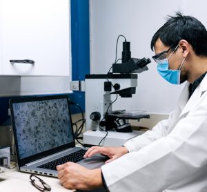 Stock photo of scientist wearing face mask using the computer and a microscopy in his lab.