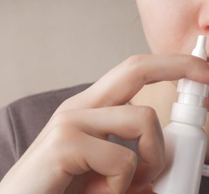A woman with a runny nose holds a nasal spray in her hand, a red nose