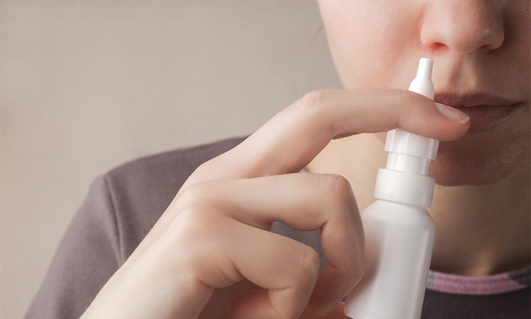 A woman with a runny nose holds a nasal spray in her hand, a red nose