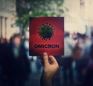 Omicron the new variant of the Covid-19 virus, coronavirus mutations, sars-cov-2 strain. Hand holds red banner warning in the crowded streets.