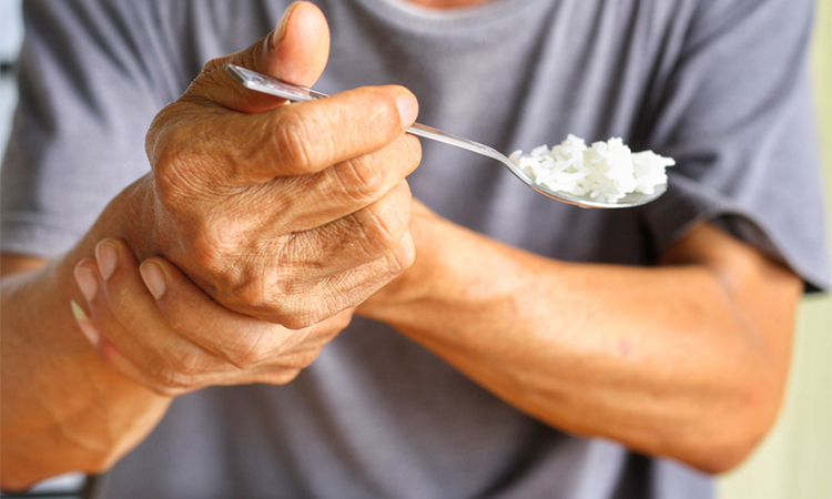 Elderly man is holding his hand while eating because Parkinson's disease.