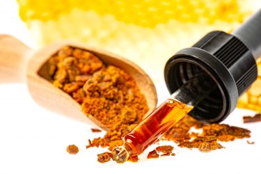 red propolis granules on a wooden spoon and a dropper containing an amber liquid (propolis tincture)