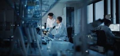 Modern Medical Research Laboratory: Two Scientists Working, Using Digital Tablet, Analyzing Test, Talking. Advanced Scientific Pharmaceutical Lab for Medicine, Biotechnology Development. Evening Time