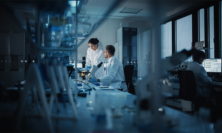 Modern Medical Research Laboratory: Two Scientists Working, Using Digital Tablet, Analyzing Test, Talking. Advanced Scientific Pharmaceutical Lab for Medicine, Biotechnology Development. Evening Time