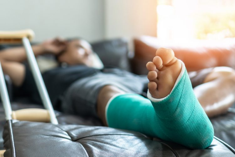 Man on sofa next to crutch with leg cast on