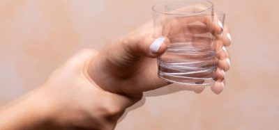 Hand of person with Parkinson's shaking while holding glass of water
