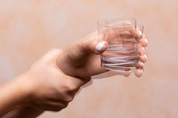 Hand of person with Parkinson's shaking while holding glass of water