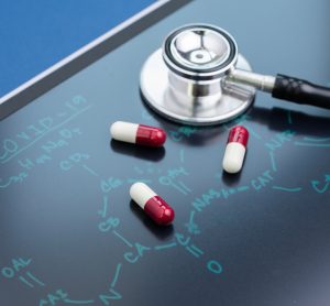 Pills and stethoscope on blackboard with COVID-19 structure written on it
