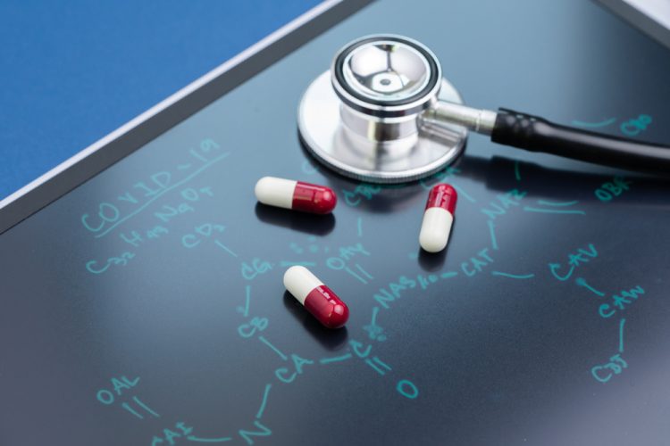 Pills and stethoscope on blackboard with COVID-19 structure written on it