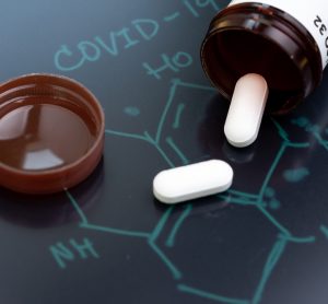 White pills on black surface with COVID-19 structure drawn on