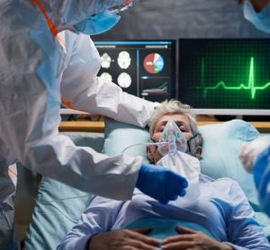 Woman in hospital bed with oxygen mask on surrounded by doctors