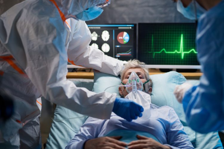 Woman in hospital bed with oxygen mask on surrounded by doctors