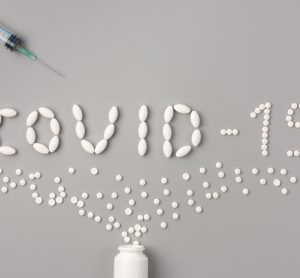 White pills spelling out COVID-19 on grey background