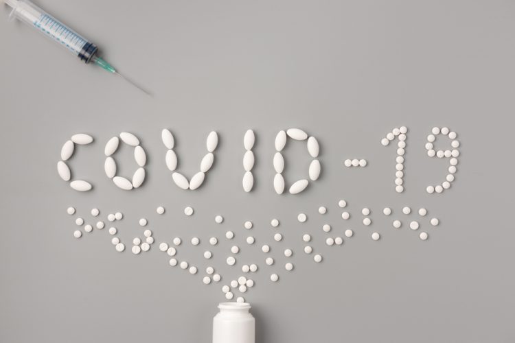 White pills spelling out COVID-19 on grey background