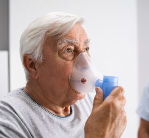 Older man with pulmonary fibrosis breathing from oxygen enhaler