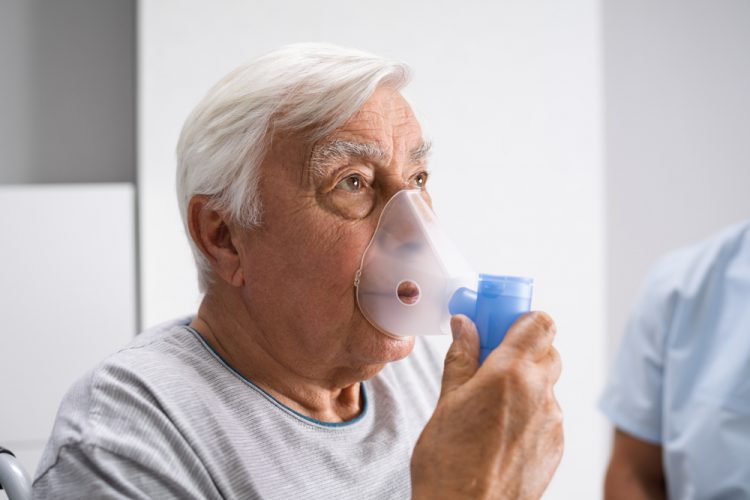 Older man with pulmonary fibrosis breathing from oxygen enhaler