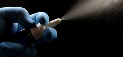 A gloved hand spraying a nasal spray, showing a fine mist against a dark background, representing innovation in nasal drug delivery technology.