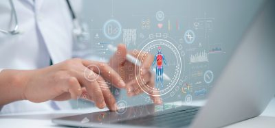 A medical researcher using a laptop with digital graphics of human anatomy, molecular data, and AI analytics overlays, symbolising the integration of artificial intelligence and biological data in drug discovery.