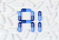 A collection of white capsules scattered on a white surface, with blue and dark blue capsules arranged in the center to form the letters 'A' and 'I'