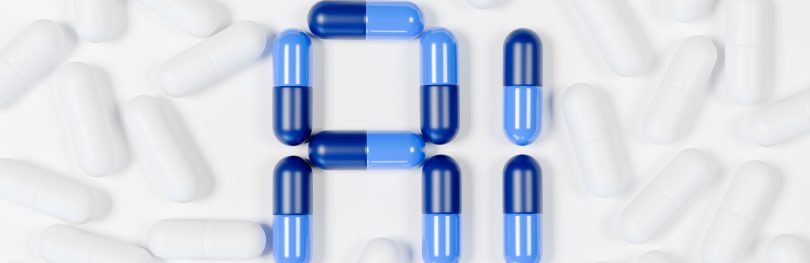 A collection of white capsules scattered on a white surface, with blue and dark blue capsules arranged in the center to form the letters 'A' and 'I'